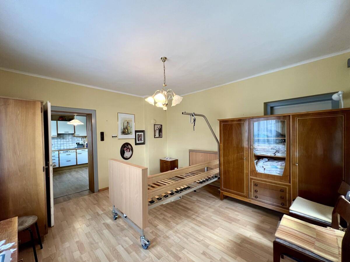 Schlafzimmer mit Pflegebett, Holzschrank und Zugang zur Küche, bietet funktionellen Wohnraum.