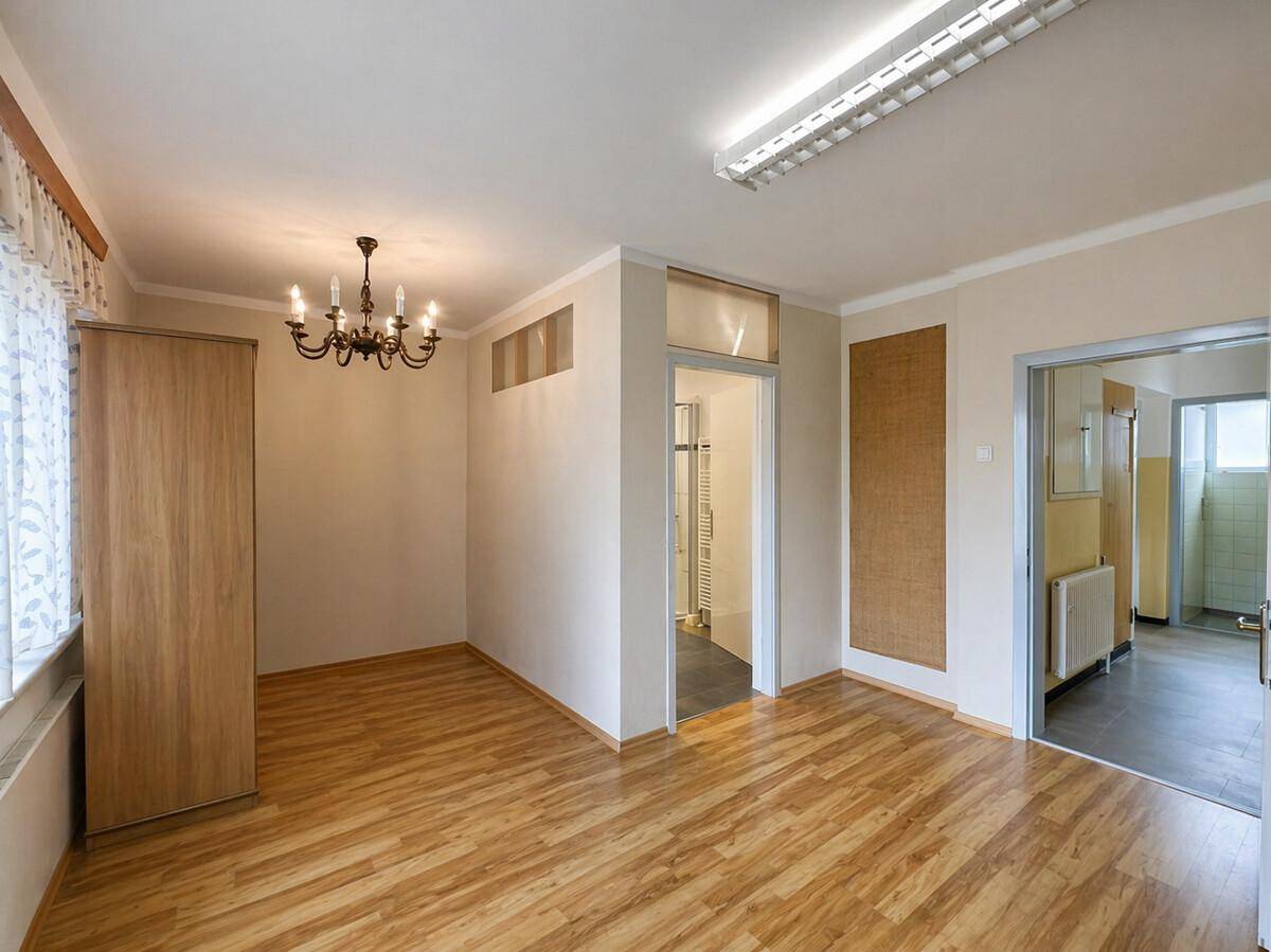 Heller Raum mit Laminatboden, Fenster und offenem Zugang zu einem Badezimmer und Flur.