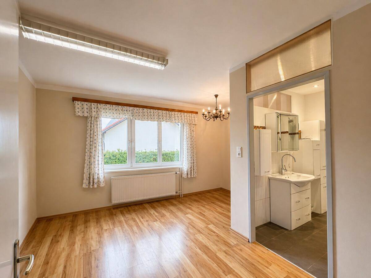 Heller Raum mit Laminatboden, großem Fenster und offenem Zugang zu einem Badezimmer.