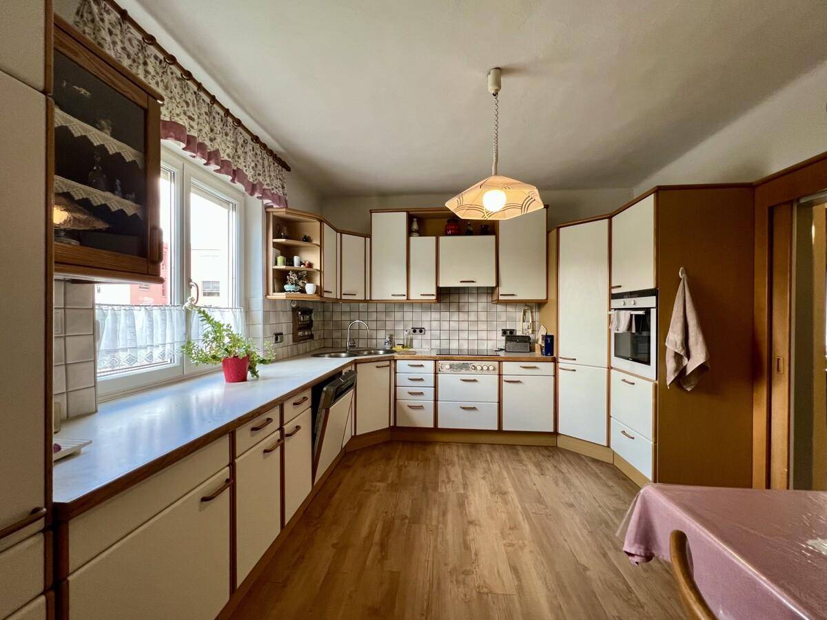 Funktionale Küche mit weißen Einbauschränken, Fliesenrückwand und Fenster mit Blick ins Grüne.