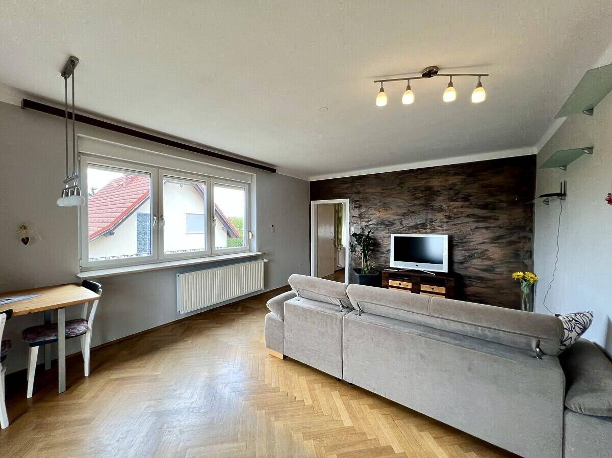 Gemütliches Wohnzimmer mit Parkettboden, Sofa und Fenster mit Blick ins Grüne.