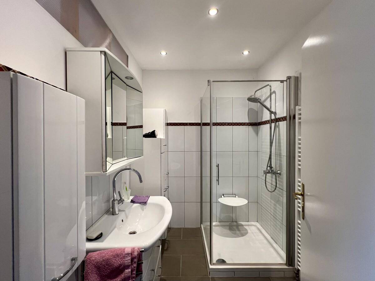 Modernisiertes Badezimmer mit Duschkabine, Waschbecken und Spiegelschrank, hell gefliest.