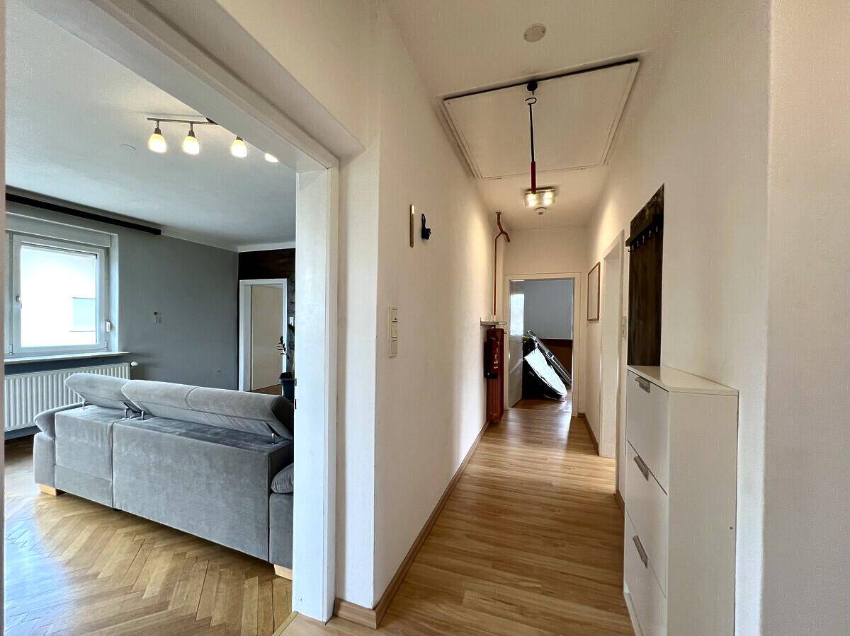 Heller Flur mit Parkettboden und Zugang zu verschiedenen Räumen, inklusive Wohnzimmer und Bad.