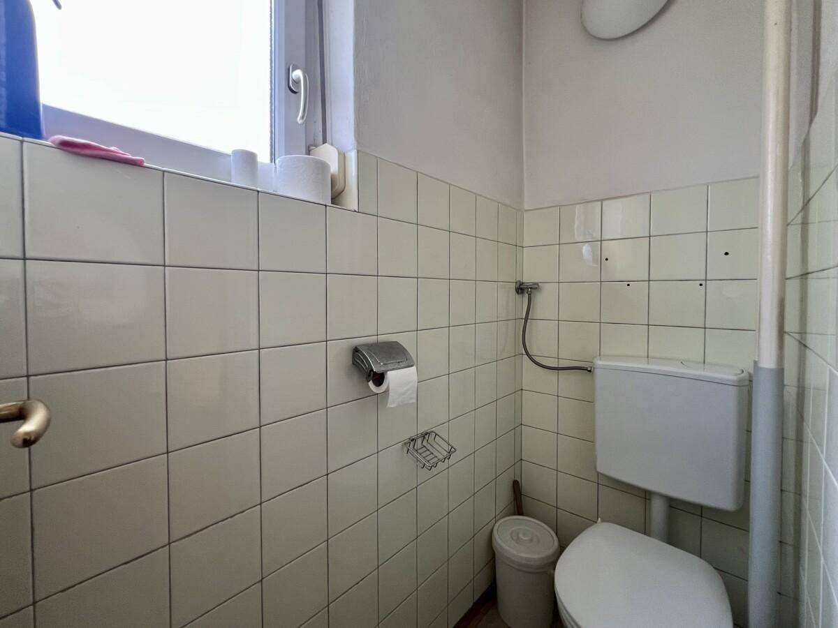 Kleines Gäste-WC mit Fenster, WC und Fliesen an den Wänden, einfach und funktional.