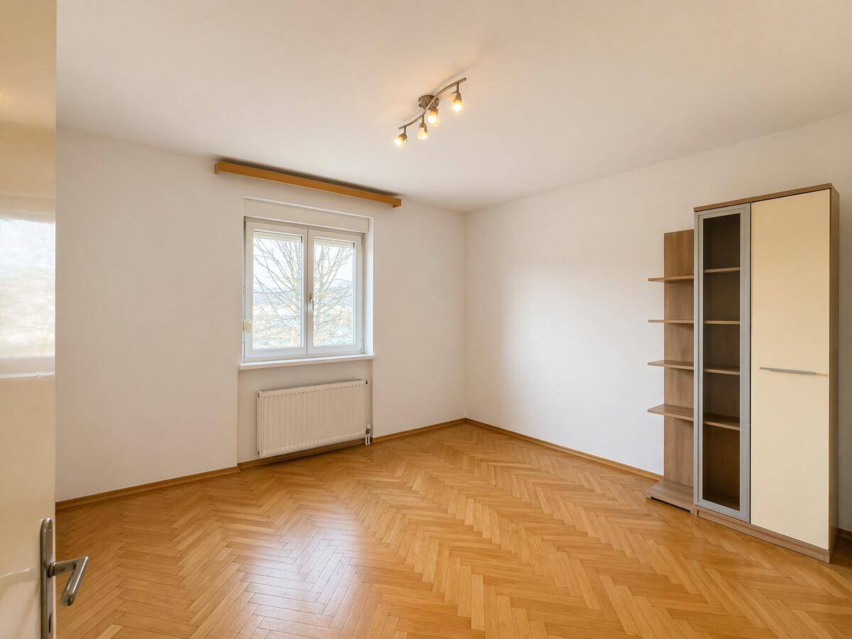 Helles Schlafzimmer mit Parkettboden, Fenster und einem modernen Kleiderschrank.