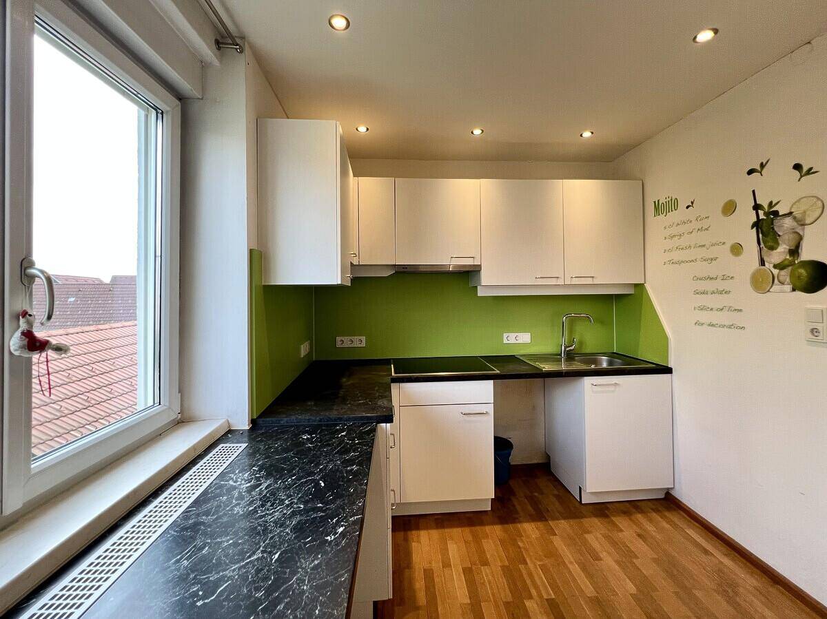 Moderne Küchenzeile mit weißen Schränken, grüner Rückwand und Fenster mit Ausblick.