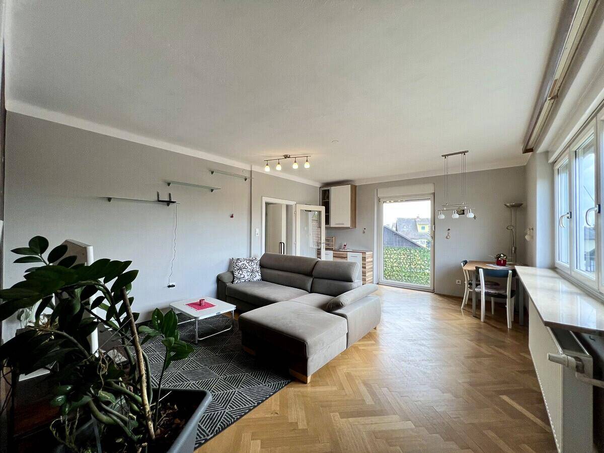 Offener Wohn- und Essbereich mit Parkettboden, Sofa und Zugang zu einem Balkon.