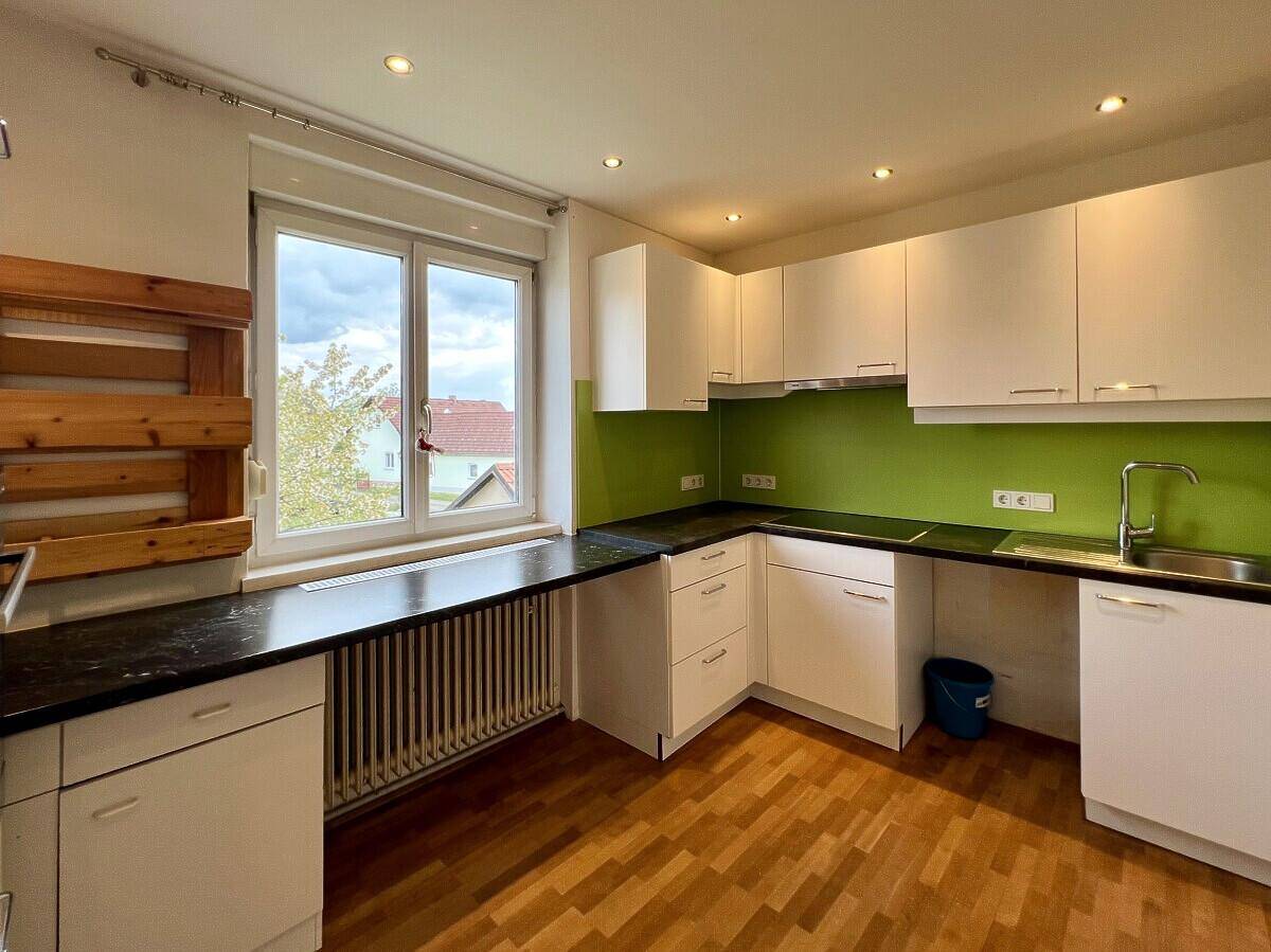 Moderne Küchenzeile mit weißen Schränken, grüner Rückwand und Fenster, das viel Licht spendet.