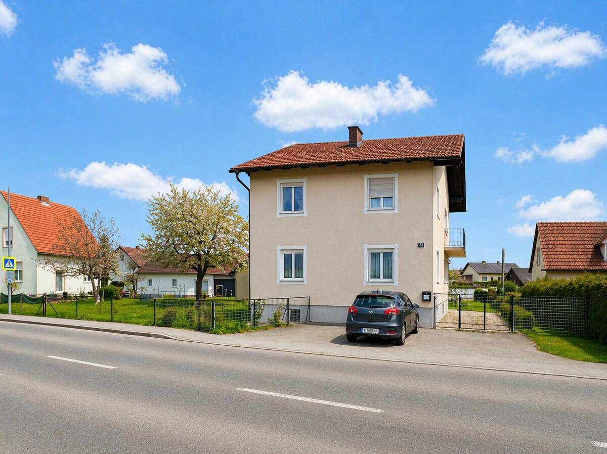 Ansicht des Hauses von der Straße aus mit Vorgarten und geparktem Auto unter blauem Himmel.