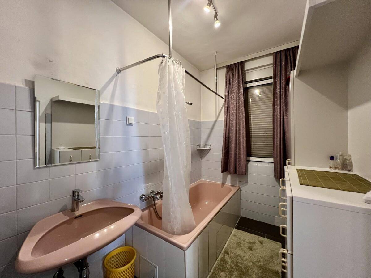 Badezimmer im 80er-Jahre-Stil mit rosa Badewanne, Waschbecken und Fenster.