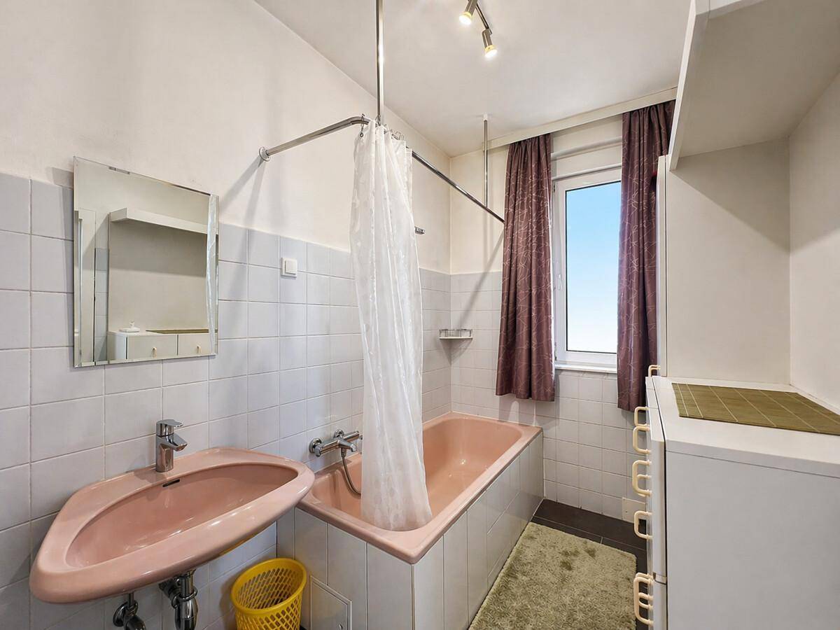 Badezimmer im 80er-Jahre-Stil mit rosa Badewanne, Waschbecken und Fenster für Tageslicht.