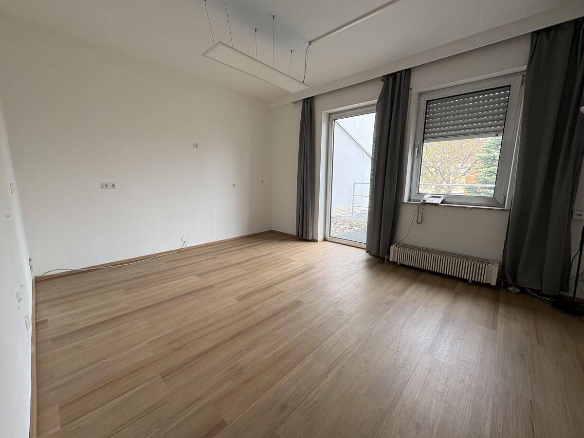 Heller Raum mit Holzboden und Zugang zu einem Außenbereich, ausgestattet mit Heizkörper.