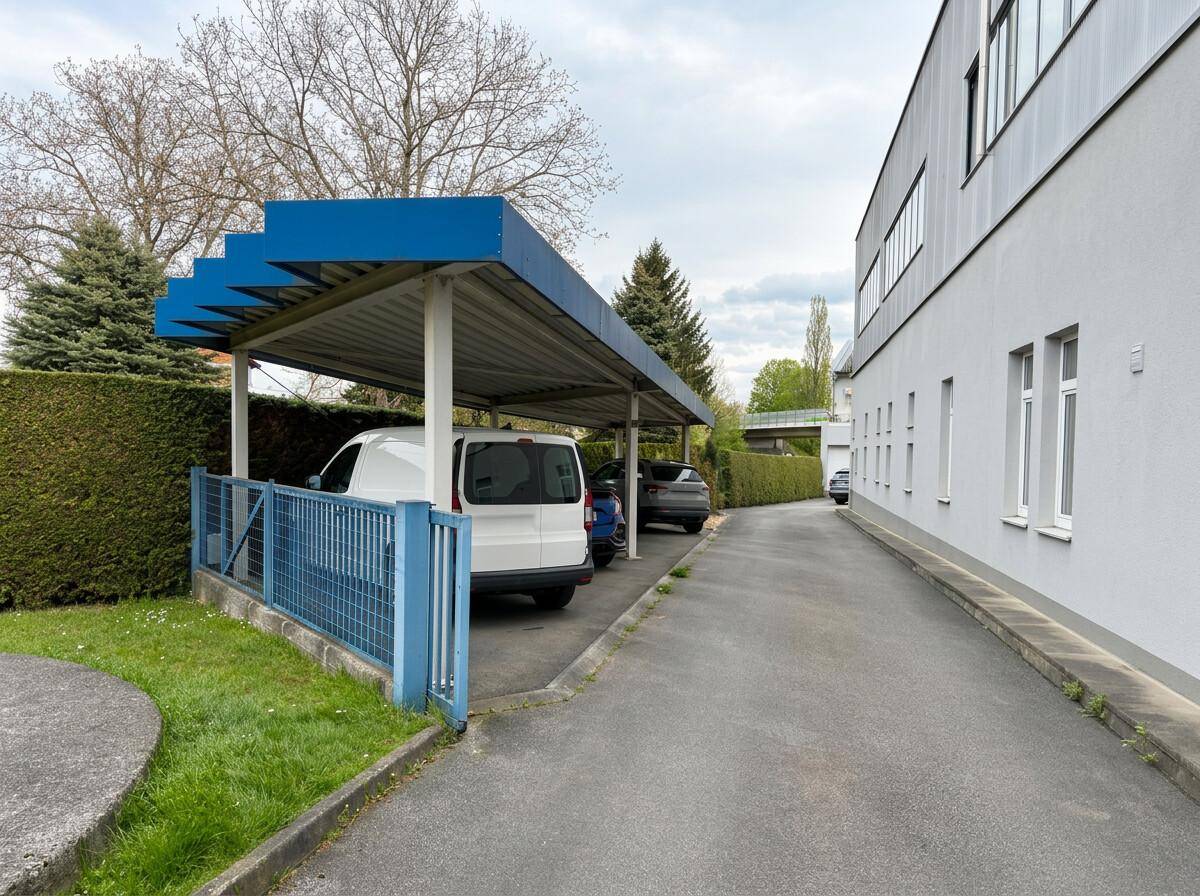 Überdachter Parkplatz (Carport) neben dem Gebäude, bietet Schutz für Fahrzeuge.