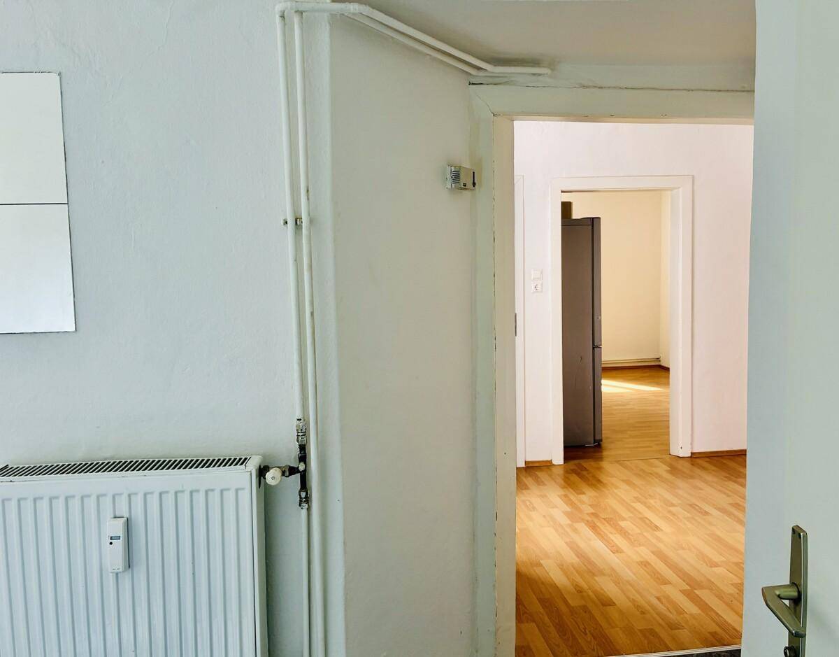 Flur mit Holzfußboden und Blick in einen angrenzenden Raum, der einen Kühlschrank zeigt.