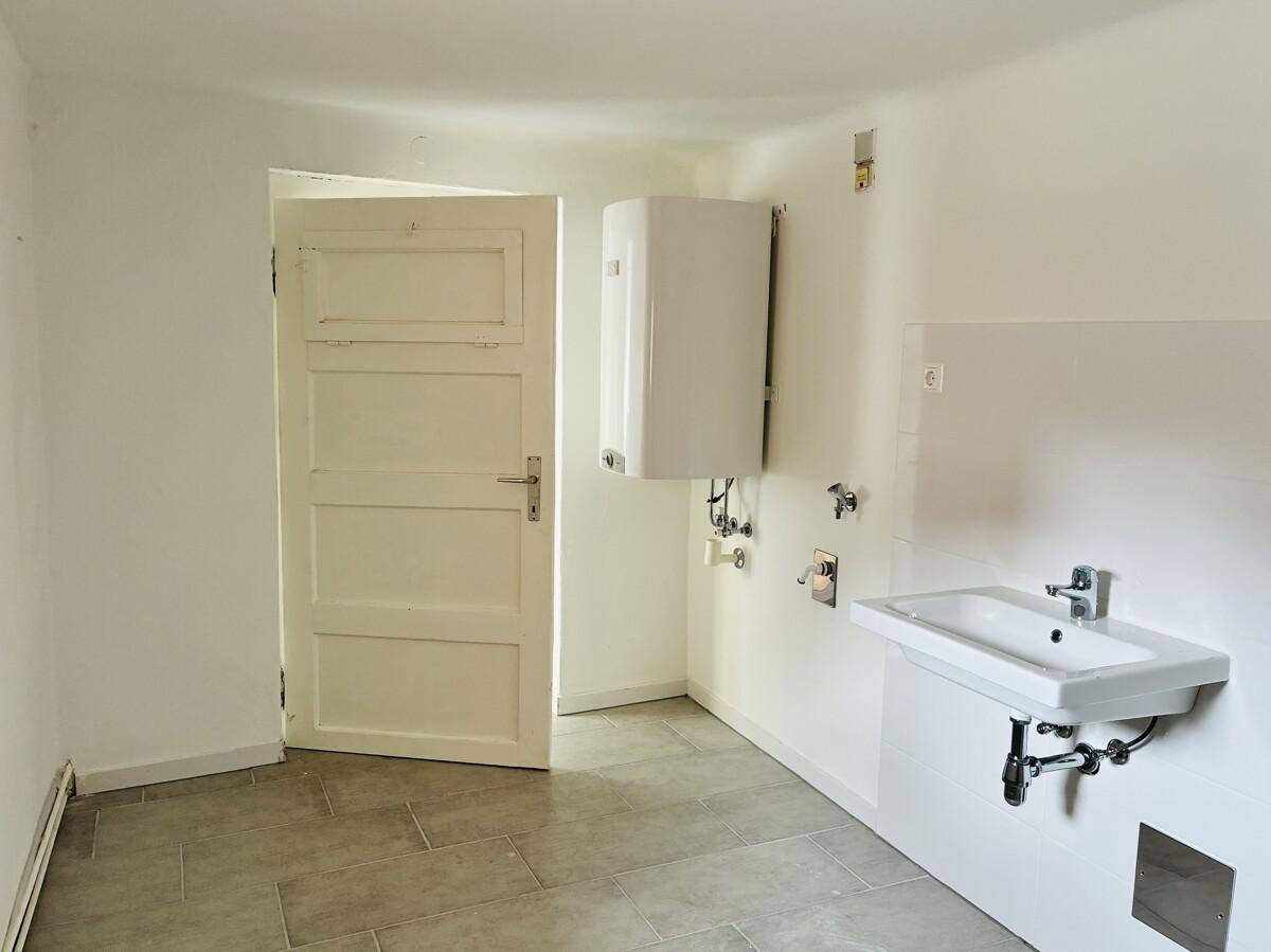 Funktionaler Raum mit Waschbecken, Warmwasserbereiter und gefliestem Boden.