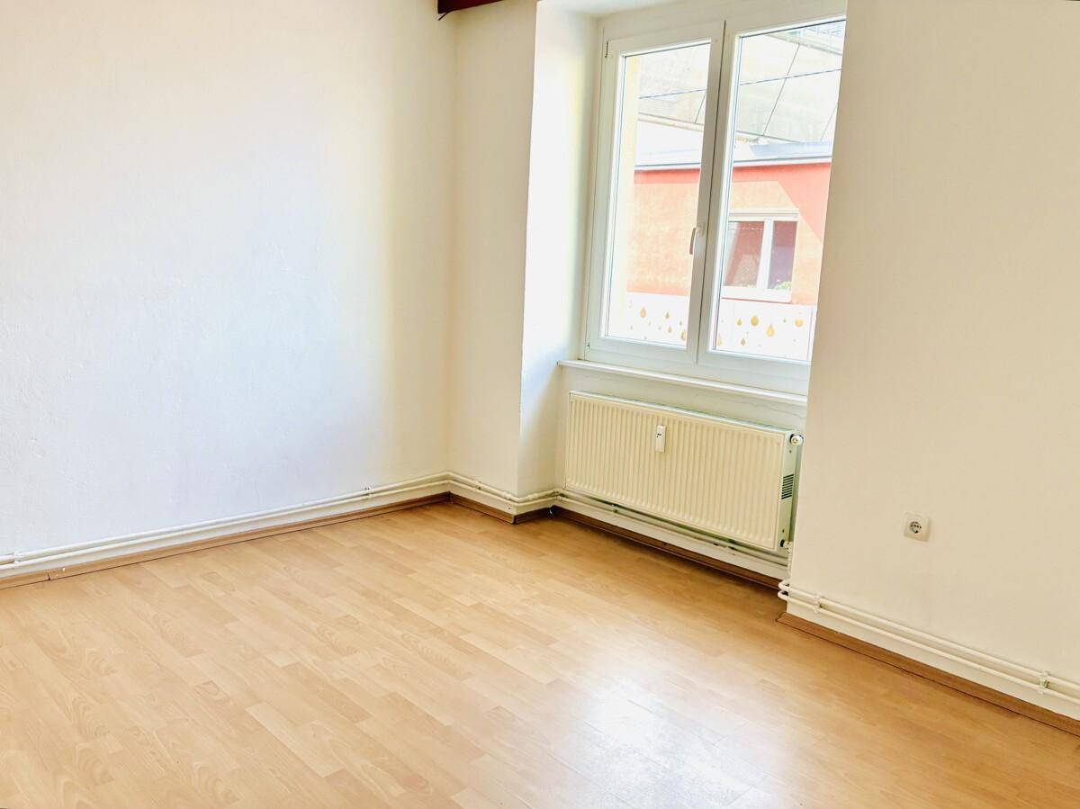Heller Raum mit Parkettboden, weißen Wänden und einem Fenster mit Blick nach draußen.