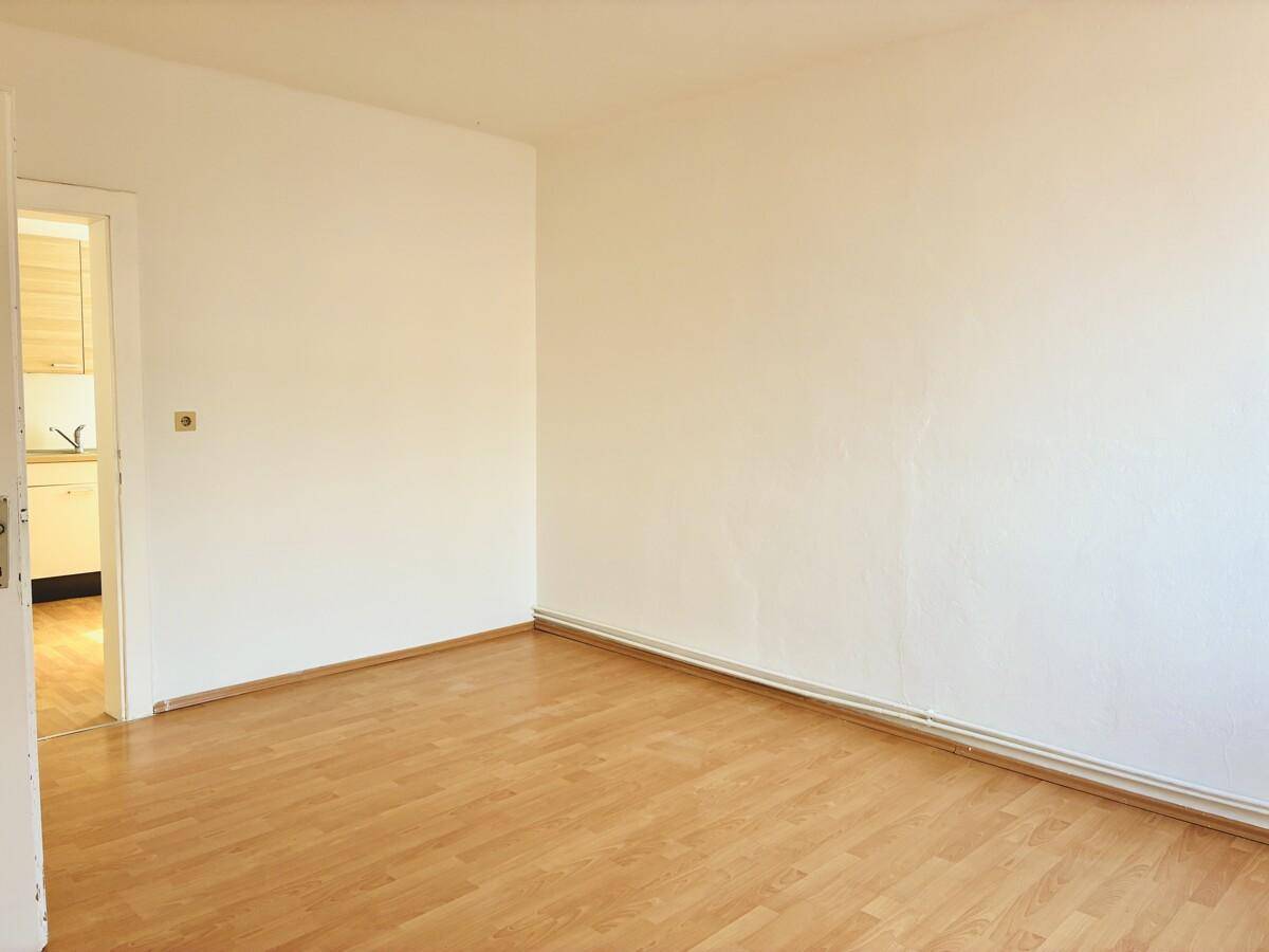 Heller Raum mit Parkettboden und Zugang zu einer angrenzenden Küche.