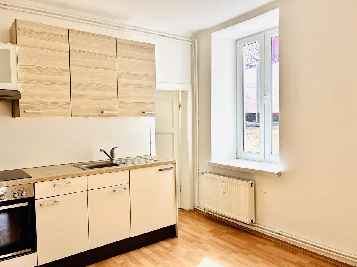 Kleine Küche mit Einbauzeile, Spüle, Kochfeld und Backofen, unter einem Fenster gelegen.