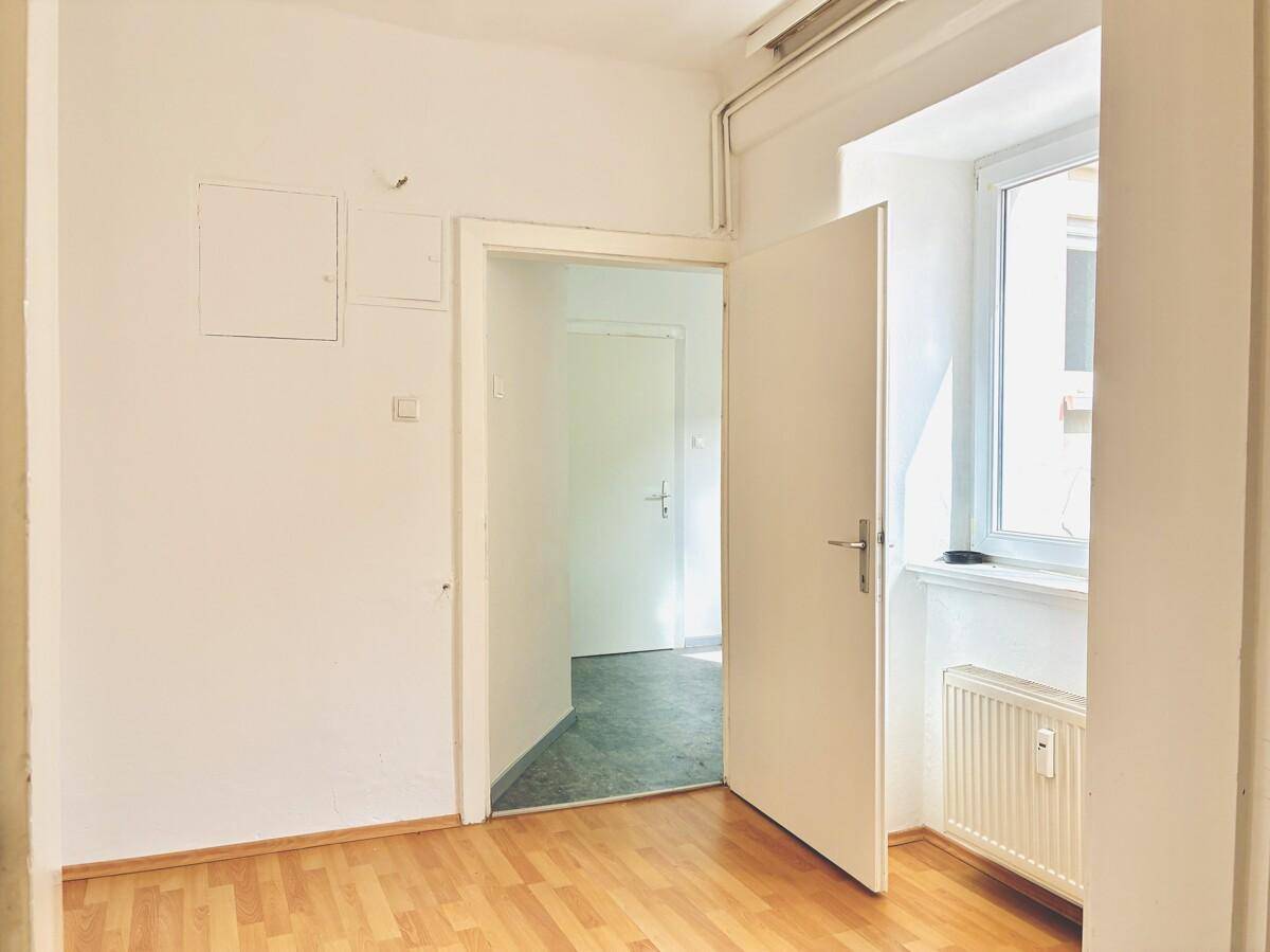 Heller Flur mit Parkettboden, weiß gestrichenen Wänden und einem Fenster mit Heizkörper.