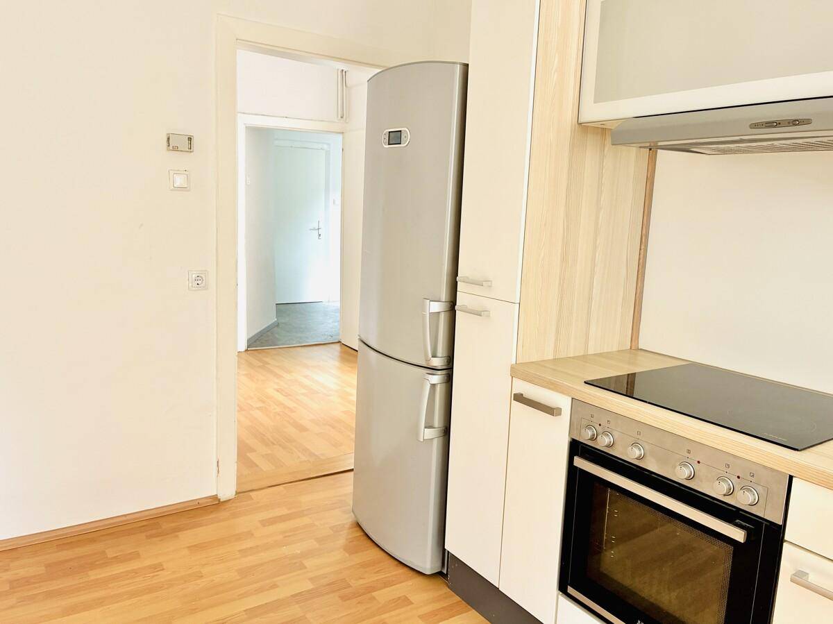 Küchenbereich mit Kühlschrank und Einbauzeile, offen zu einem angrenzenden Raum.