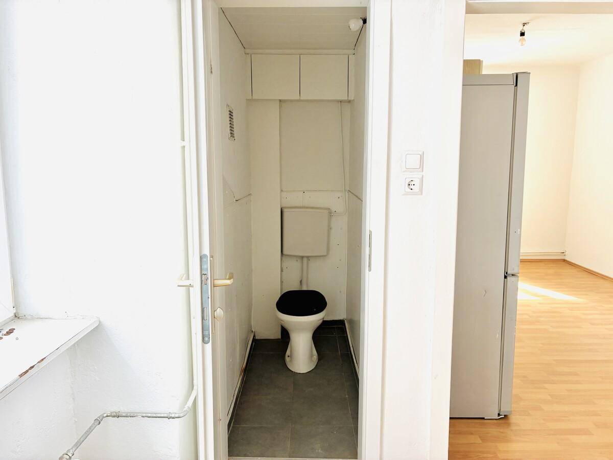 Separate Toilette mit dunklem Fliesenboden und weiß gestrichenen Wänden.