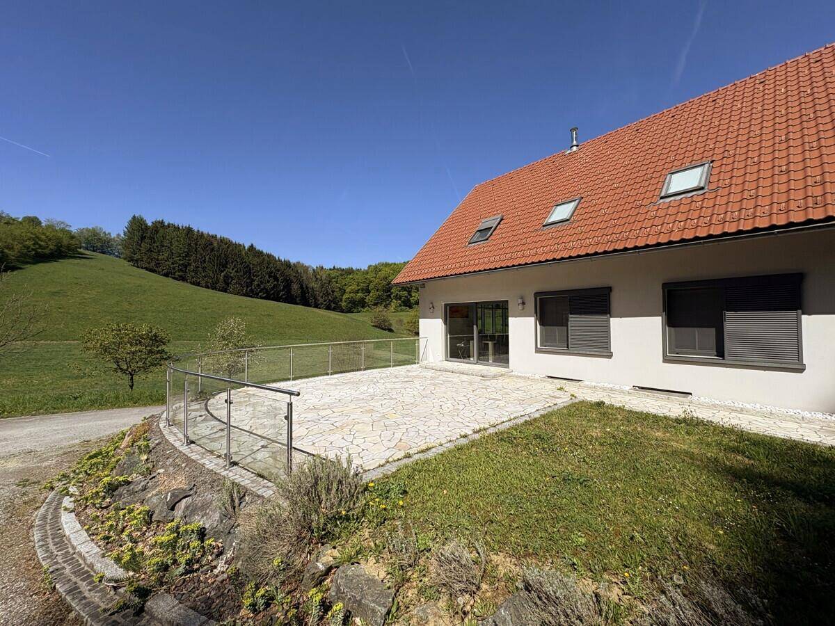 Geräumige Steinterrasse mit Glasgeländer und weitem Blick auf die grüne Hügellandschaft.
