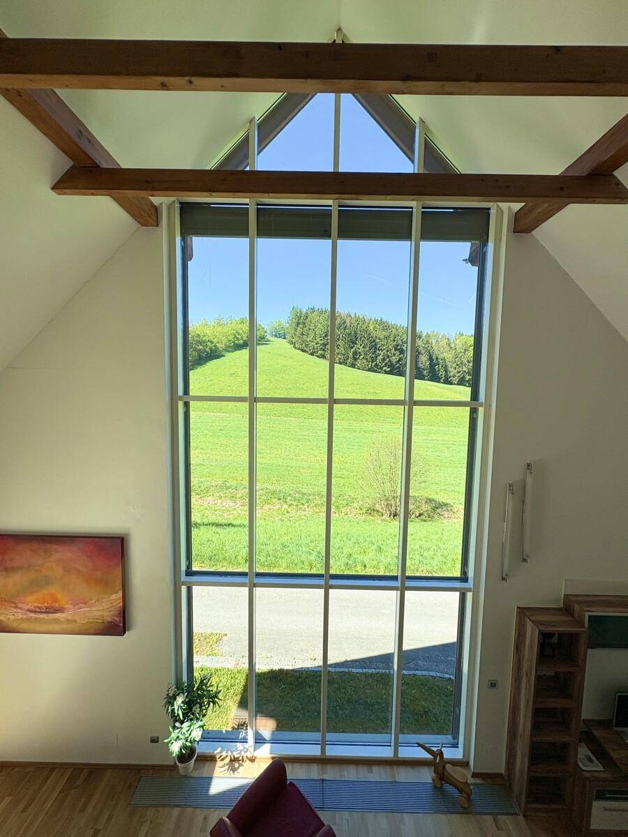 Hohe Fensterfront im Wohnzimmer bietet einen beeindruckenden Blick auf die grüne Hügellandschaft.