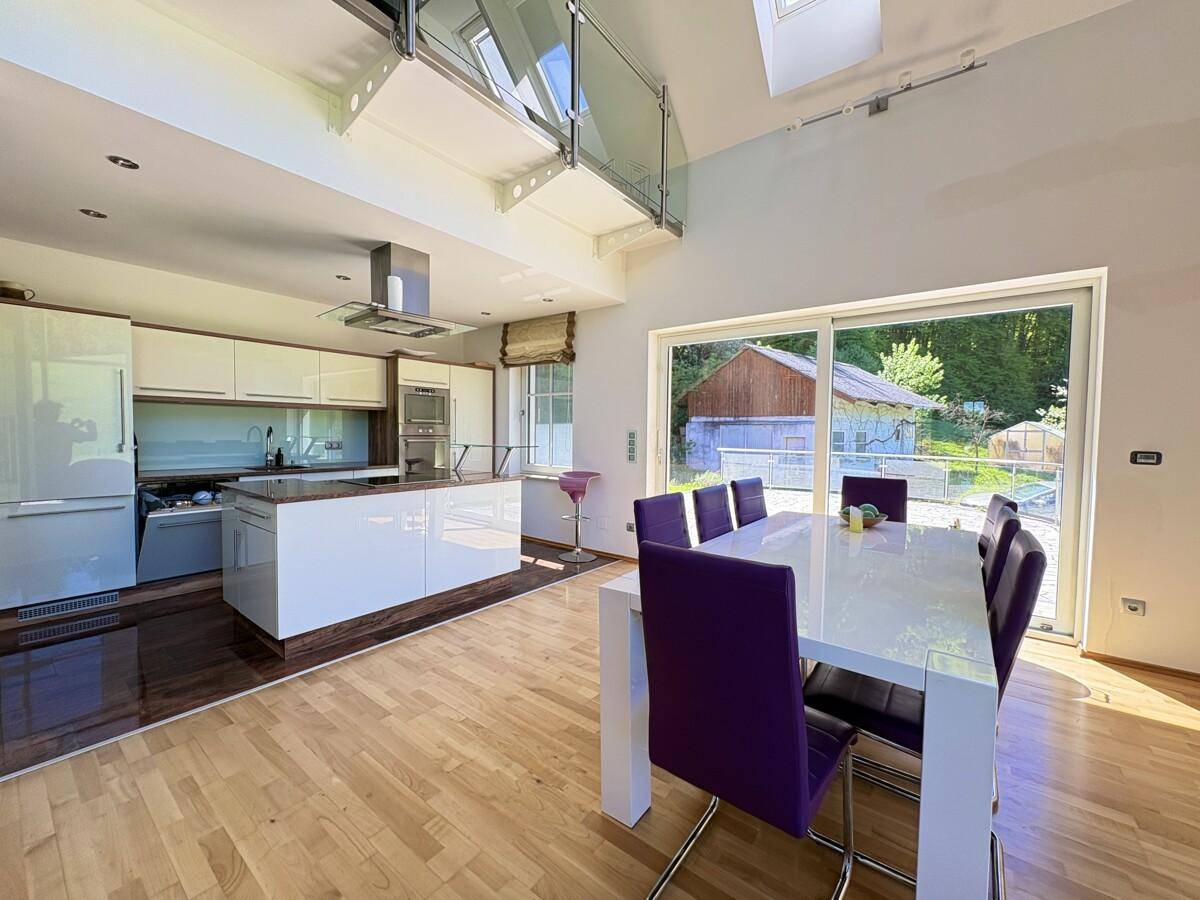 Moderne offene Küche mit weißen Hochglanzfronten, Kücheninsel und Essbereich mit Terrassenzugang.
