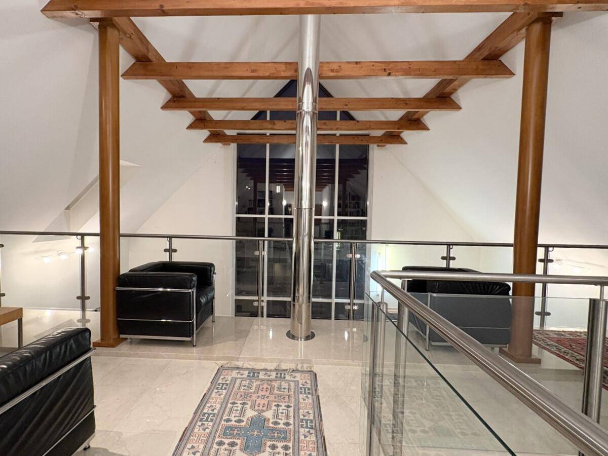Offene Galerie mit Glasgeländer, Holzbalken und Sitzgelegenheiten, die den Wohnbereich überblickt.