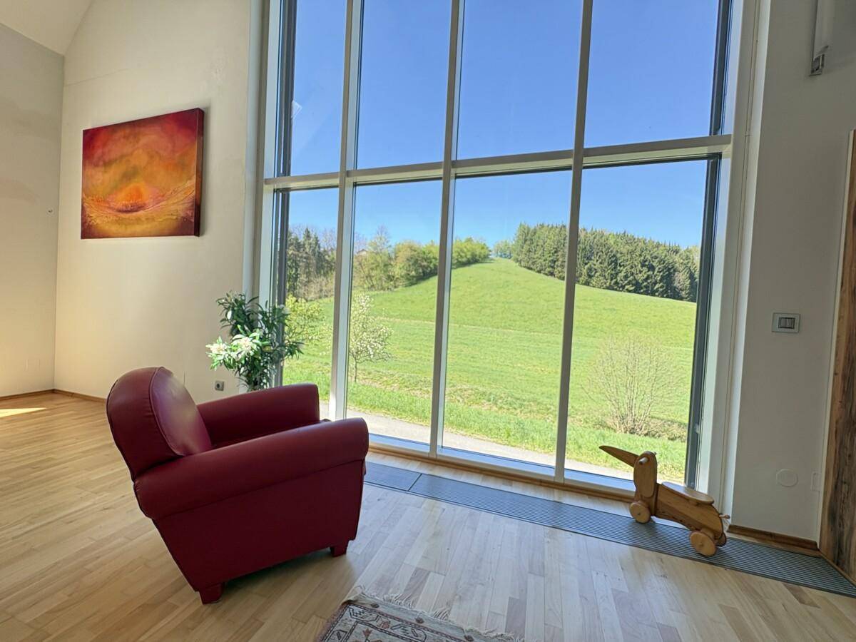 Gemütlicher Sessel vor der großen Fensterfront mit weitem Blick auf die grüne Landschaft.