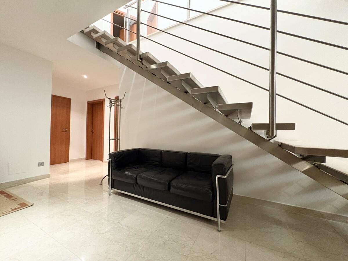 Heller Eingangsbereich mit moderner Treppe, schwarzem Sofa und Marmorboden.