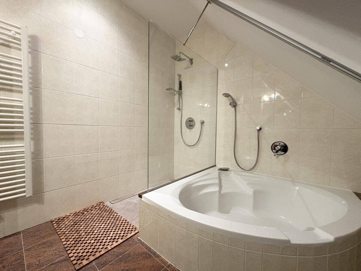Modernes Badezimmer mit Eckbadewanne, Dusche und beheiztem Handtuchhalter unter Dachschräge.