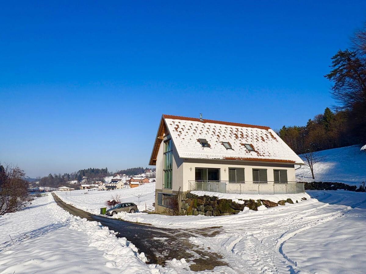 Modernes Haus im Winter mit schneebedecktem Dach und Umgebung unter blauem Himmel.