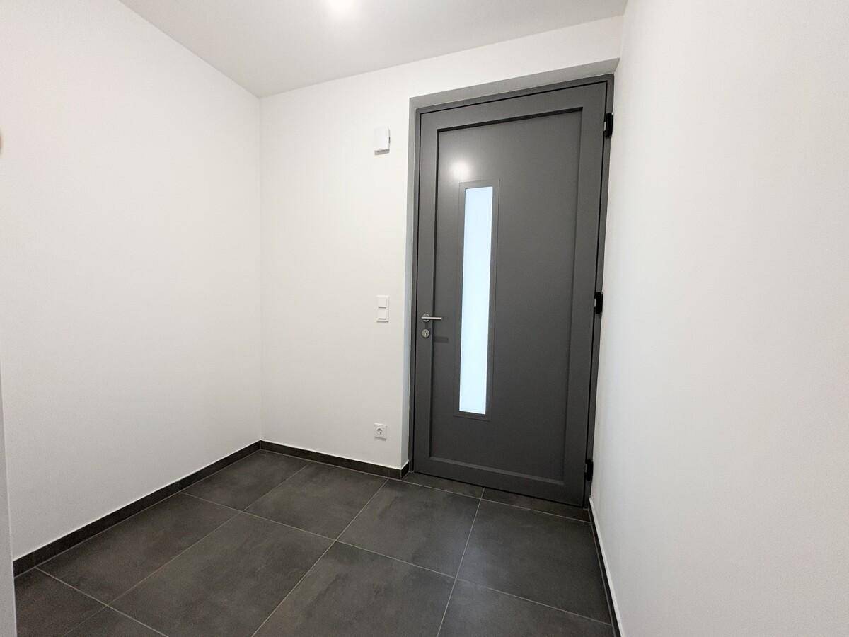 Heller Eingangsbereich mit moderner grauer Tür und dunklen Bodenfliesen.