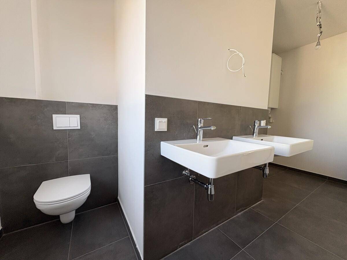 Geräumiges Badezimmer mit zwei modernen Waschbecken, wandhängendem WC und dunklen Fliesen.