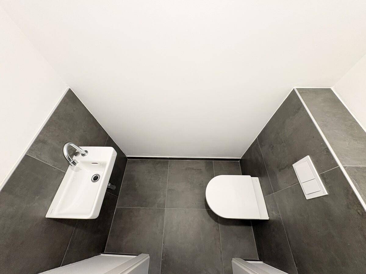 Modernes Gäste-WC mit dunklen Fliesen, wandhängendem WC und kleinem Waschbecken.