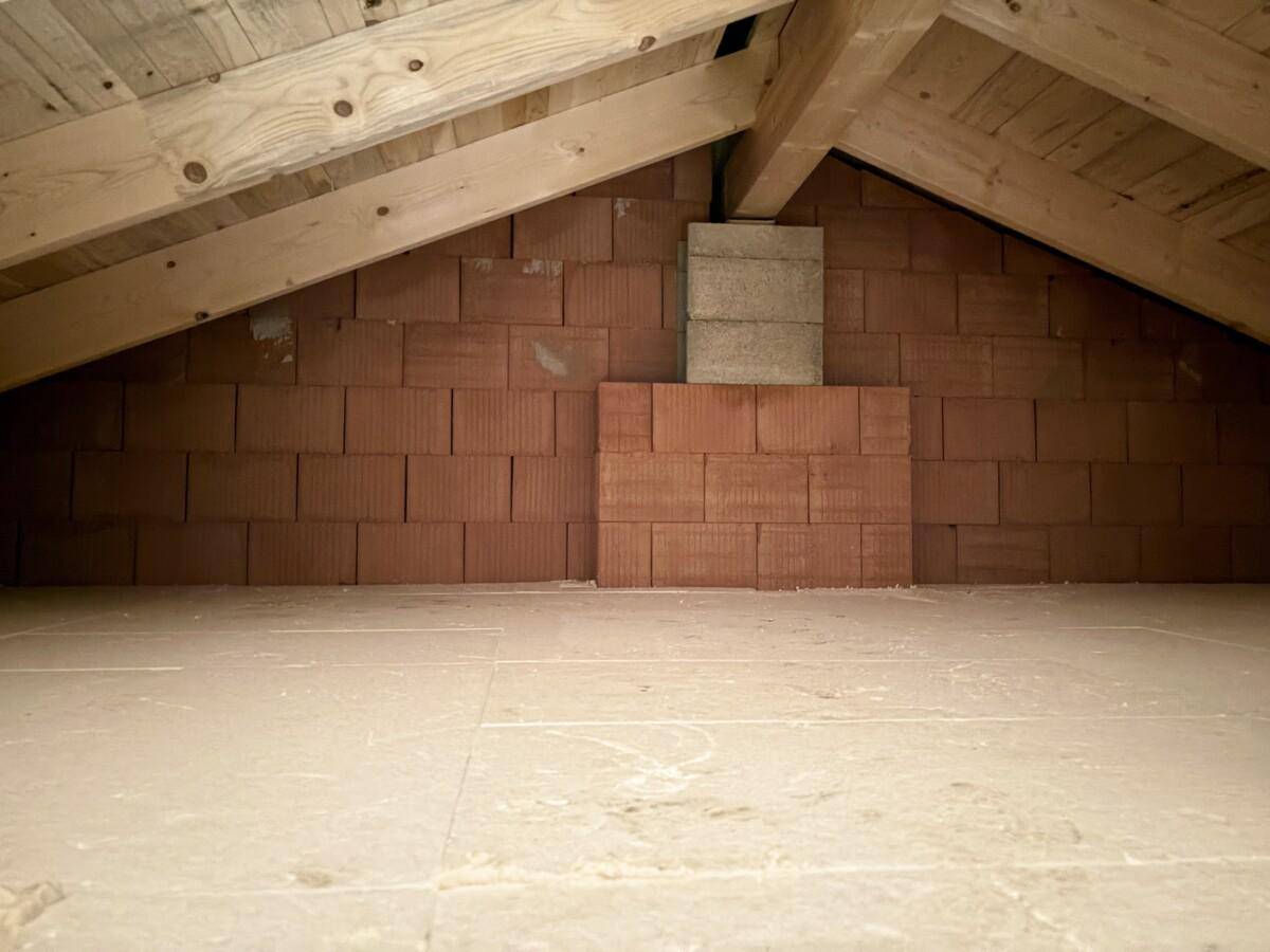 Unausgebauter Dachboden mit sichtbaren Holzbalken und Ziegelwänden, bietet Ausbaupotenzial.