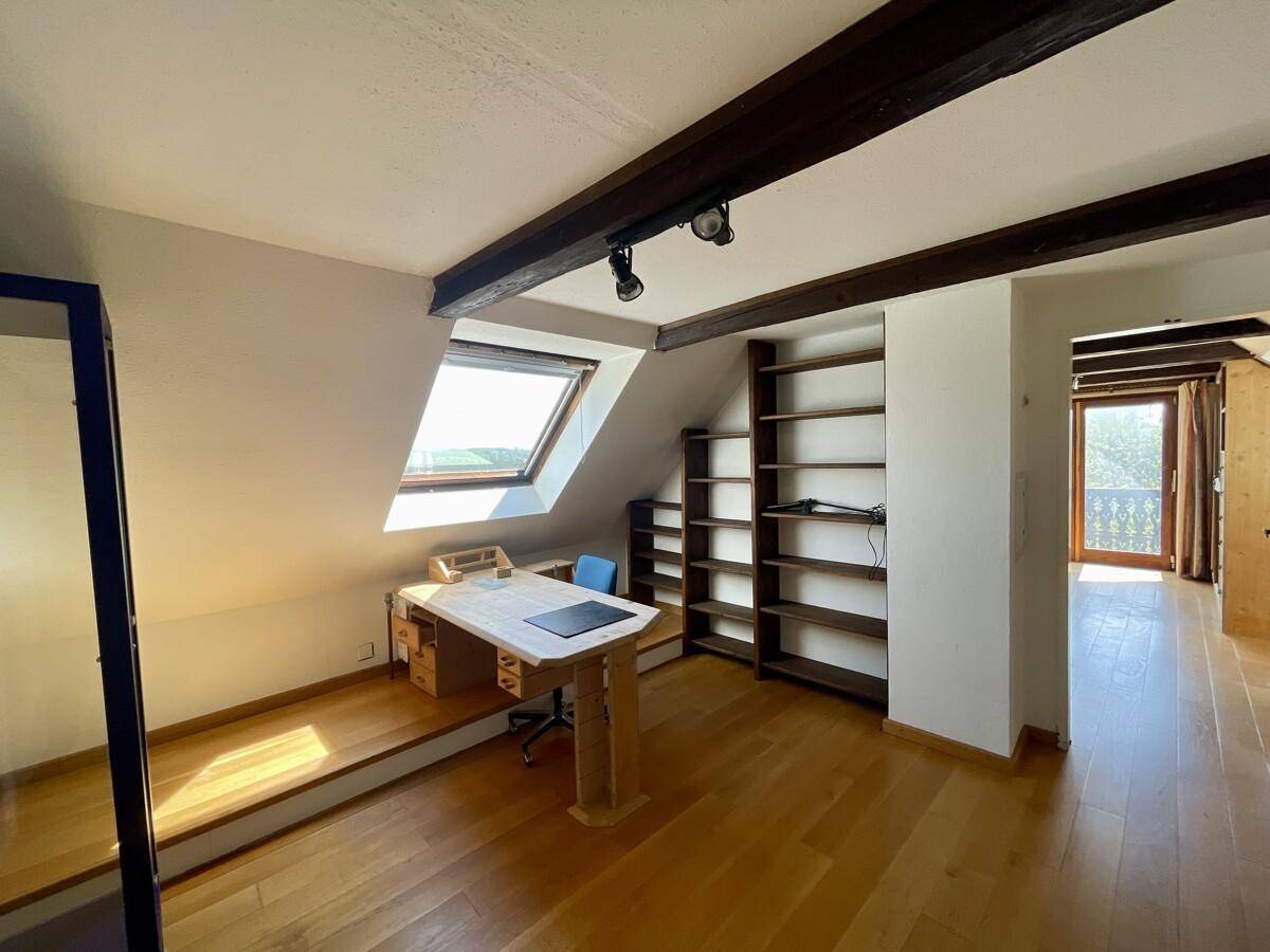 Helles Dachgeschossbüro mit Holzboden, Einbauregalen und einem Dachfenster, das viel Licht hereinlässt.