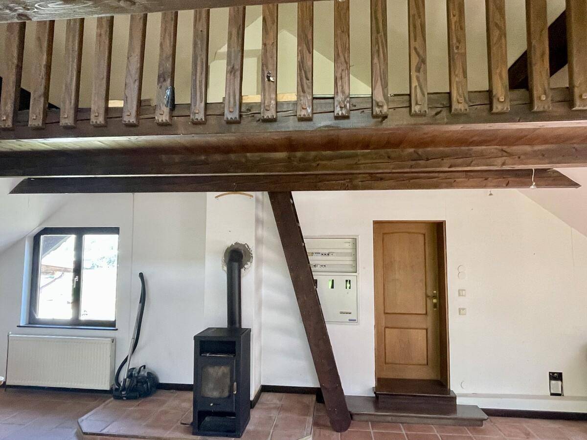 Detailansicht eines modernen Holzofens in einem Dachgeschosszimmer mit Terrakottafliesen und Fenster.