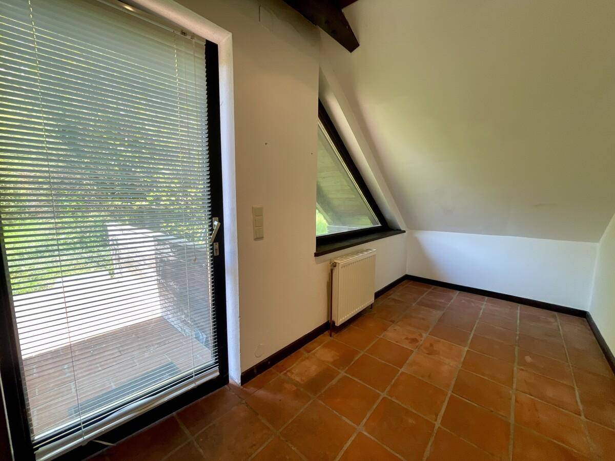 Leerer Raum mit Terrakottafliesen und einer großen Glastür, die zu einem Außenbereich führt.