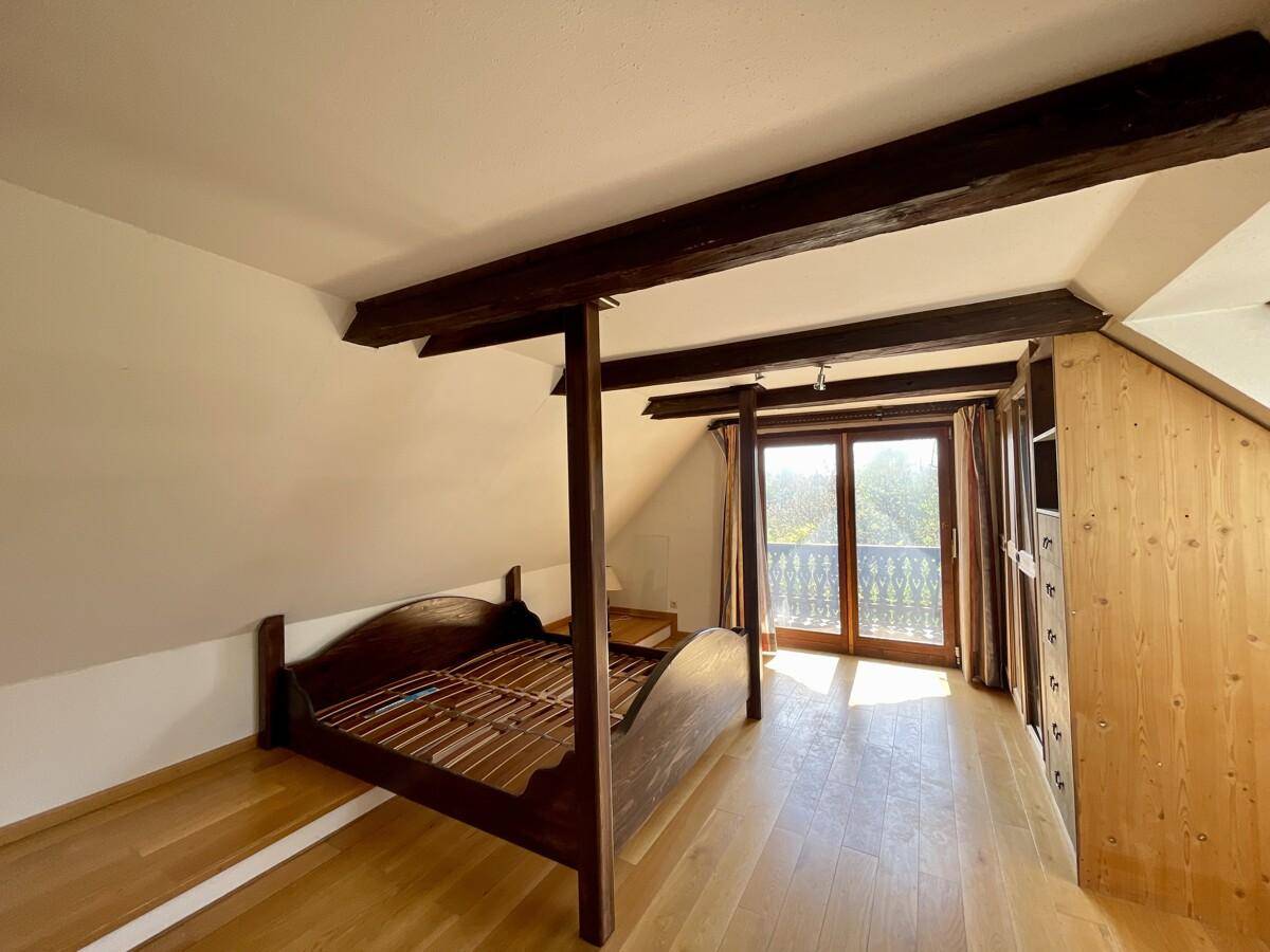 Gemütliches Dachgeschoss-Schlafzimmer mit Holzboden, Holzbalken und direktem Zugang zu einem Balkon.