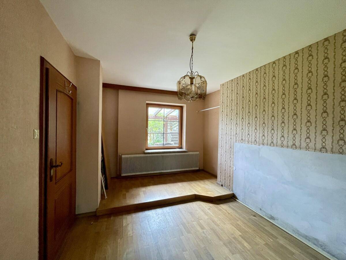 Raum mit Holzboden, gemusterter Tapete und Fenster, renovierungsbedürftig.