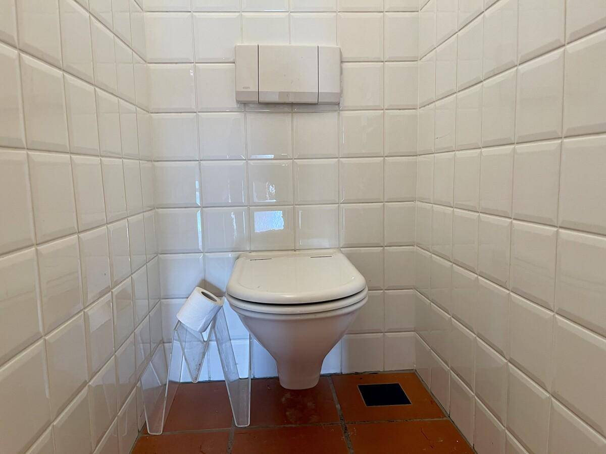 Kleines WC mit weißen Fliesen und Terrakotta-Boden.