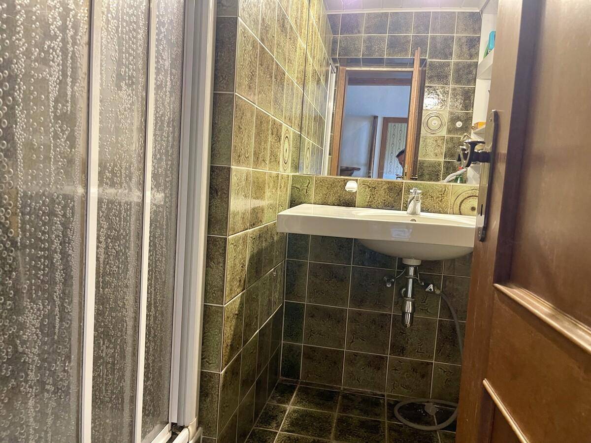 Badezimmer mit grünen Fliesen, Duschkabine und Waschbecken mit Spiegel.