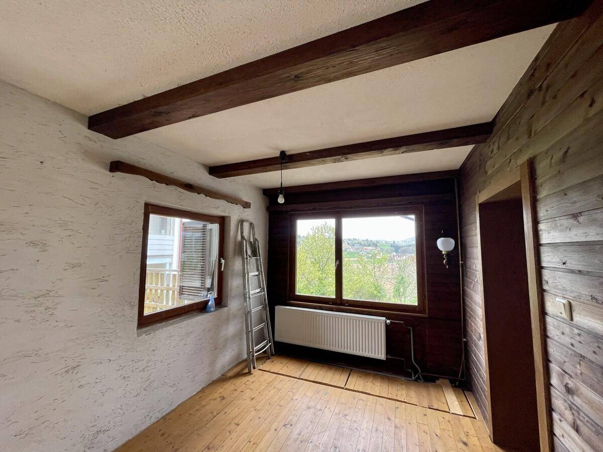Zimmer mit Holzboden, sichtbaren Deckenbalken und Holzvertäfelung an einer Wand.
