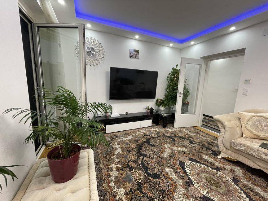Wohnzimmer mit großem Fernseher, Pflanzen und Zugang zu einem weiteren Raum.