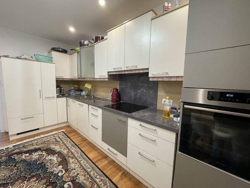 Moderne Küche mit weißen Schränken, dunklen Arbeitsplatten und integriertem Backofen.