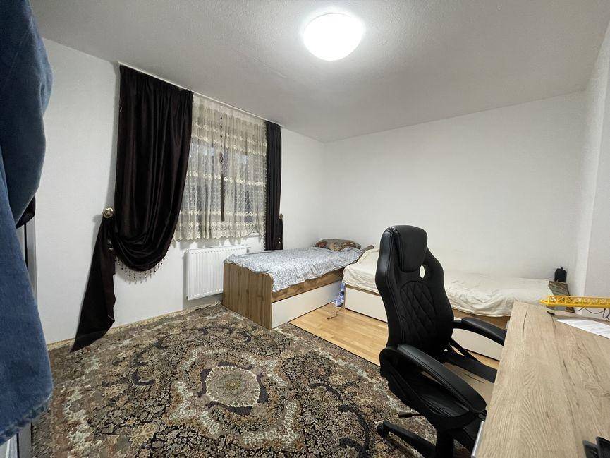 Schlafzimmer mit zwei Einzelbetten, Schreibtischstuhl und Fenster mit dunklen Vorhängen.