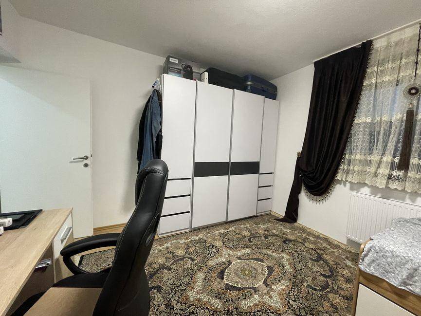 Schlafzimmer mit großem Kleiderschrank, Schreibtischstuhl und Fenster mit dunklen Vorhängen.