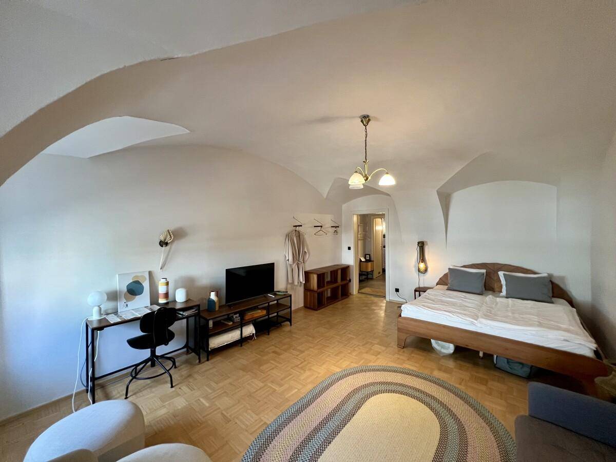 Geräumiges Schlafzimmer mit Parkettboden, Gewölbedecke und Schreibtisch.